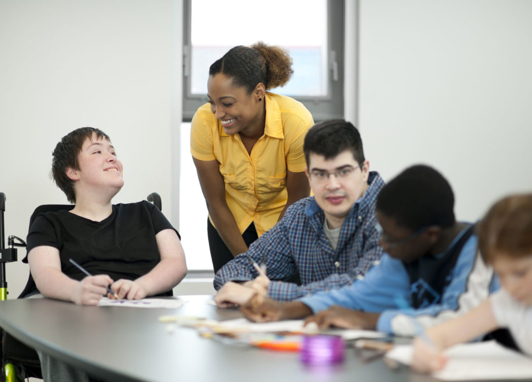 A diverse group of students with disabilities sit at a table and work on arts and crafts
