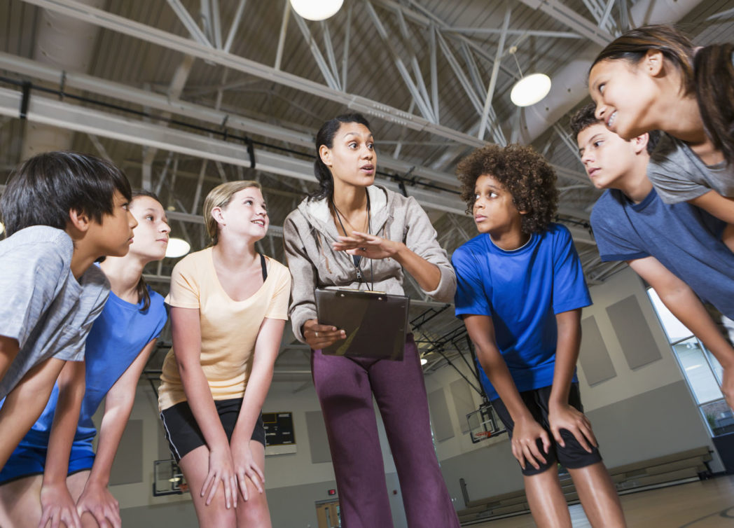 group of children with coach huddled-up in school gym